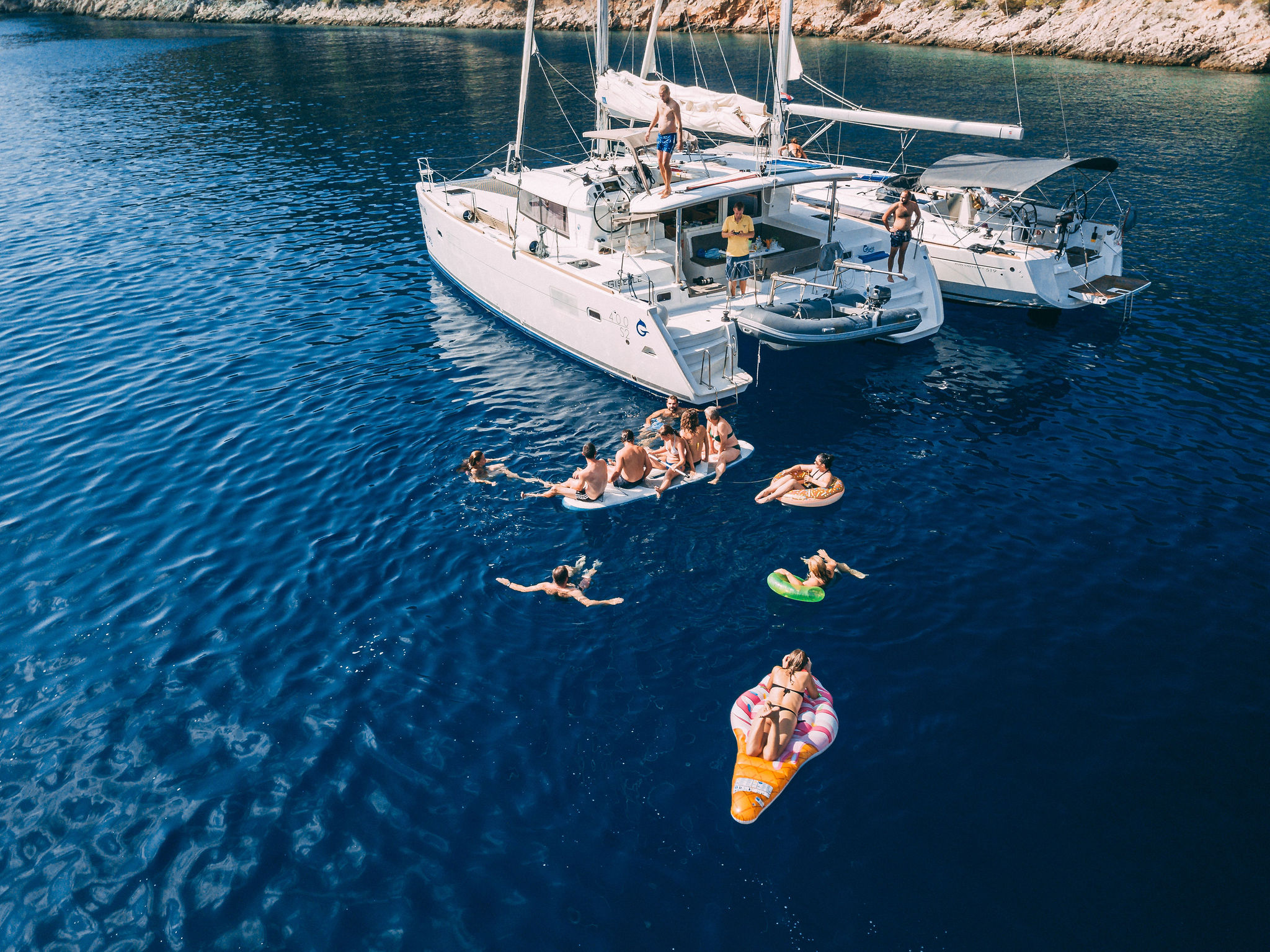 Aerial drone view of two catamarans with guests swimming and floaties in turquoise Adriatic water, yacht party by Cosmic Production