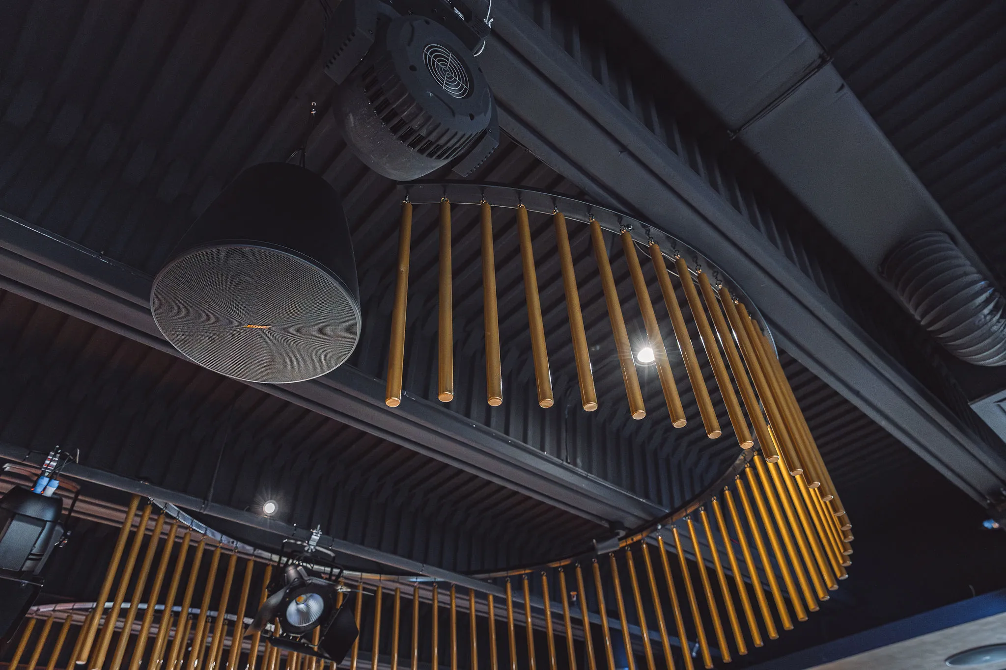 Bose pendant speaker with orange logo mounted near a gold chandelier in a hotel interior