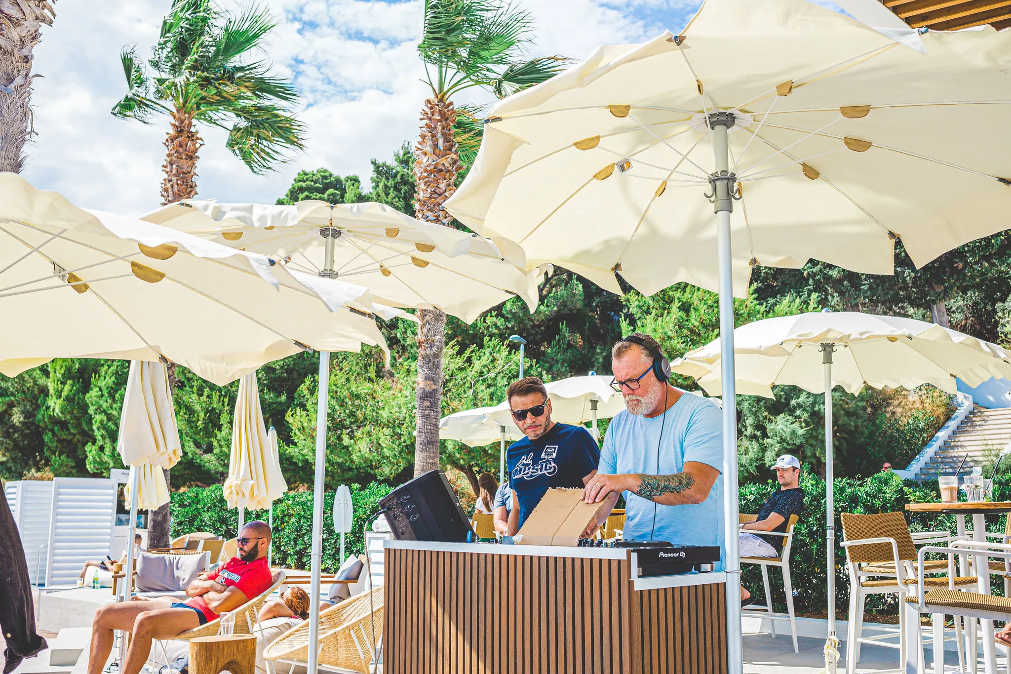 Two DJs performing a B2B set at an Adriatic beach club pool area with palm trees — Cosmic Production resort entertainment