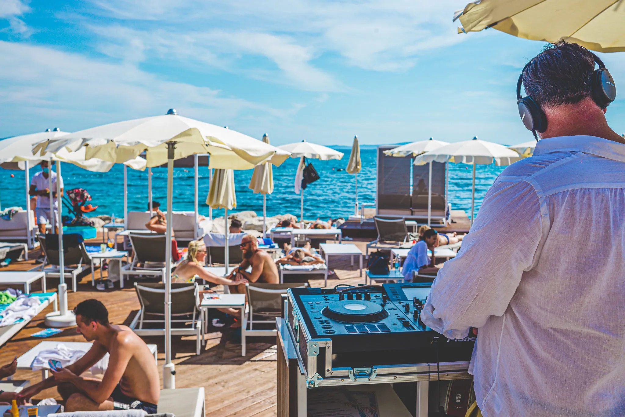 DJ performing behind the decks overlooking beach crowd at Mistral Beach Club