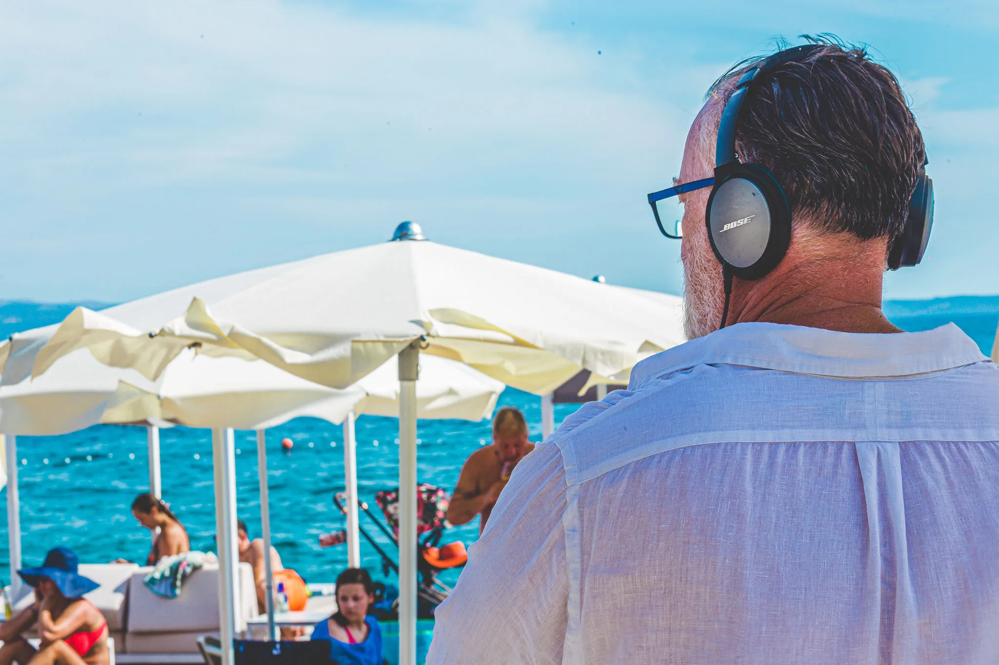 DJ performing at beach club with Bose headphones overlooking the turquoise Adriatic — Cosmic Production