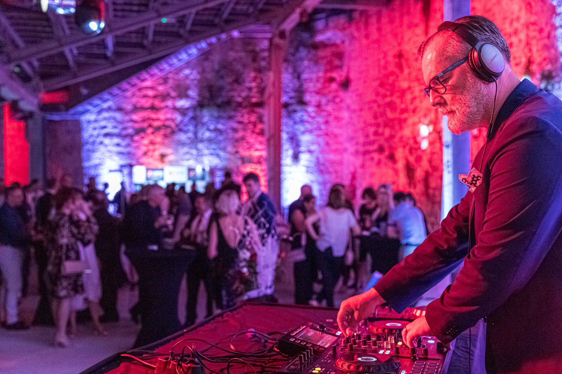 DJ performing at corporate gala with full AV lighting production on fortress stone walls