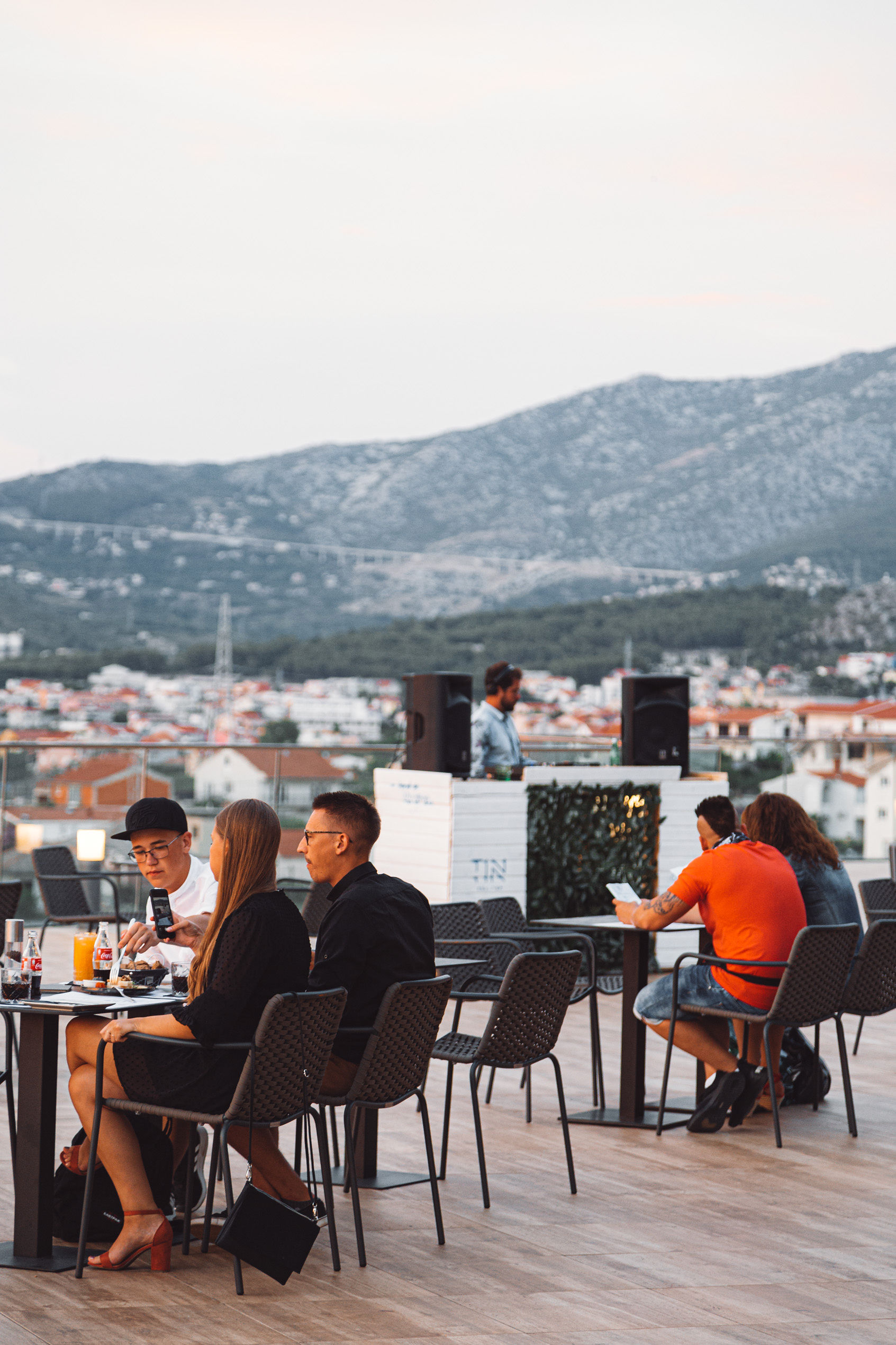 Guests dining at TIN Rooftop with DJ Leo in the background, Split mountains behind at golden hour