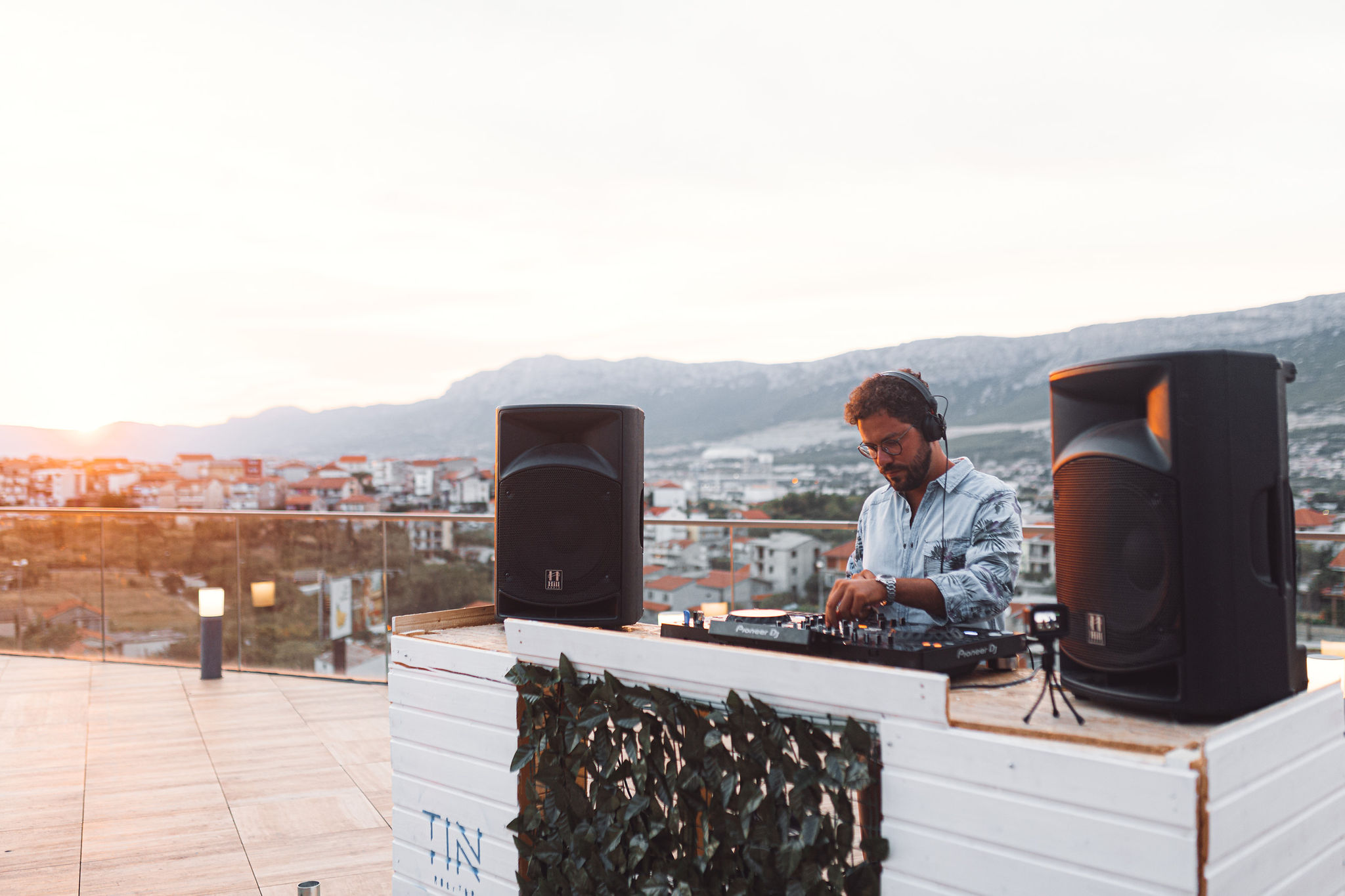 DJ Leo performing at Pioneer DJ setup at TIN Rooftop with Split mountains at golden hour