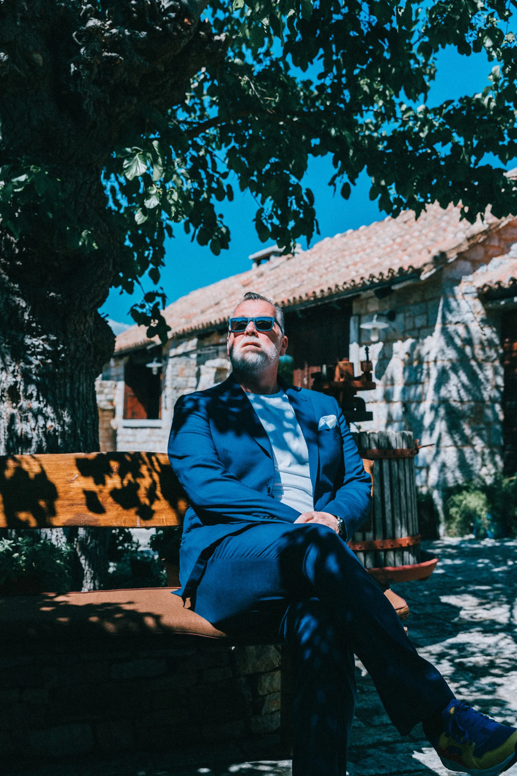DJ Matthew Bee portrait in blue suit seated at a Croatian stone village — Cosmic Production founder