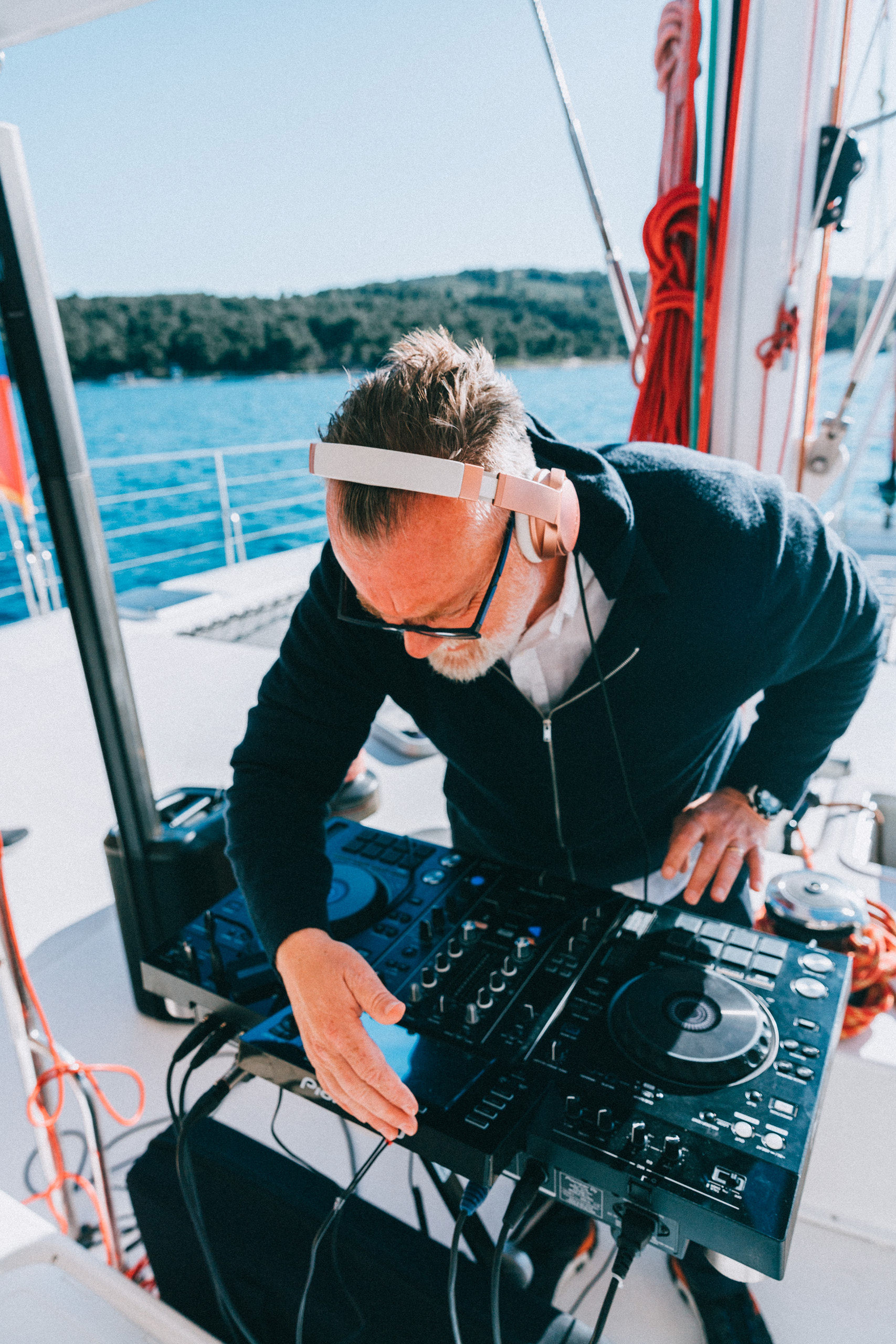 DJ Matthew Bee performing with headphones at Pioneer DJ controller on yacht with Adriatic sea behind
