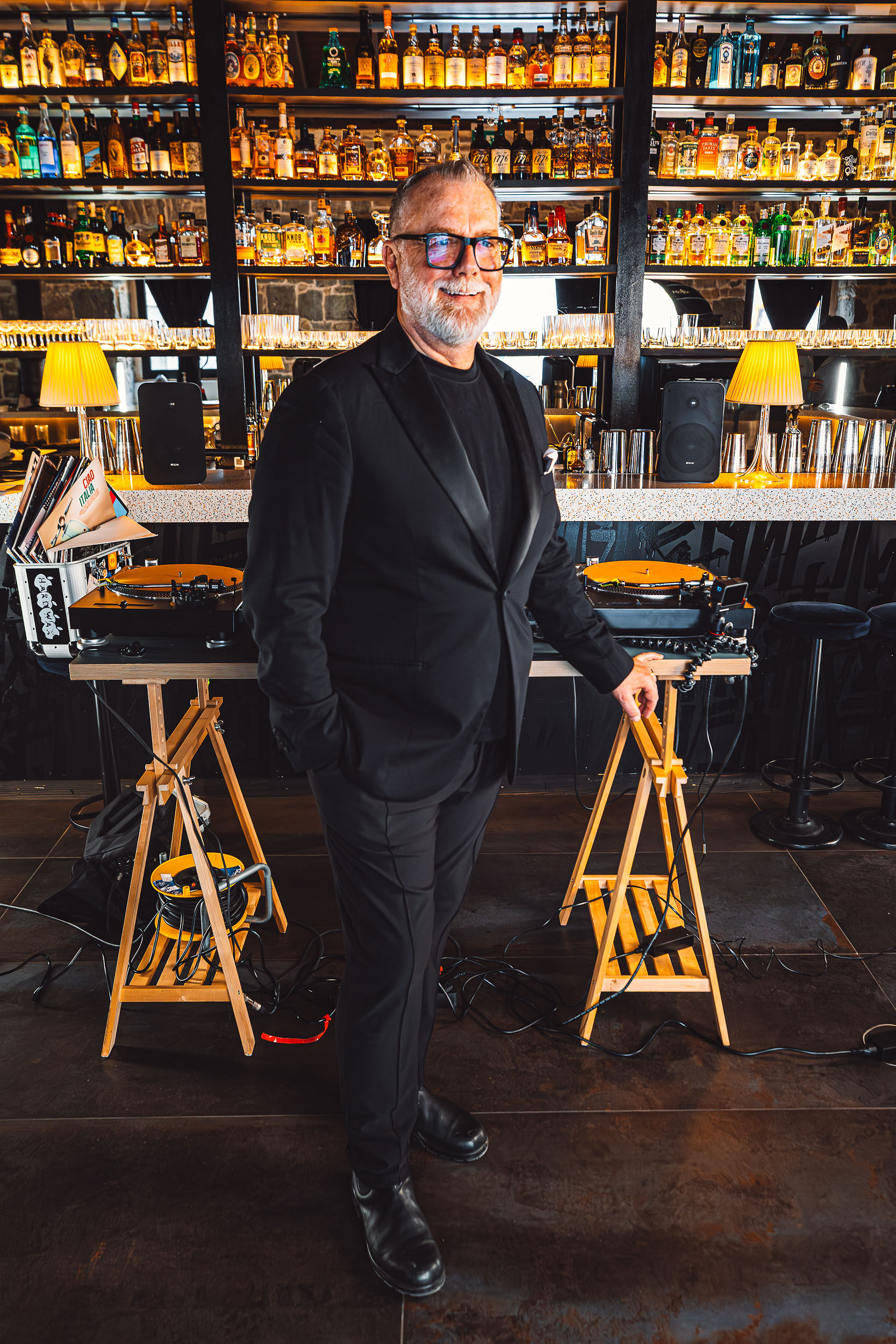 DJ in suit performing with vinyl turntables, K-Gear speakers visible on bar counter at Bar Sistema Split