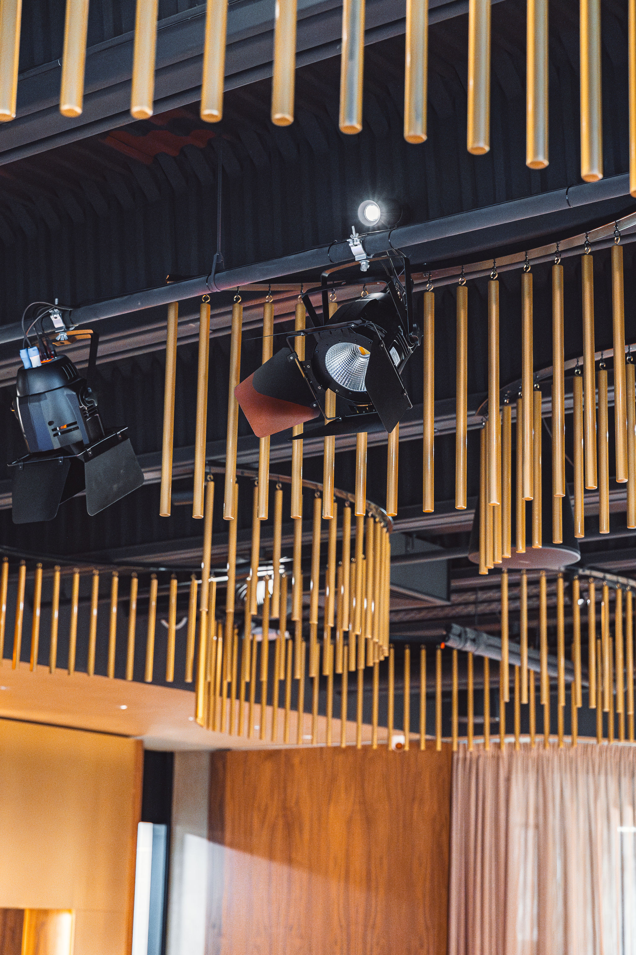 Fresnel theatrical spotlights mounted on ceiling rail alongside gold chandeliers at Level Restaurant Split