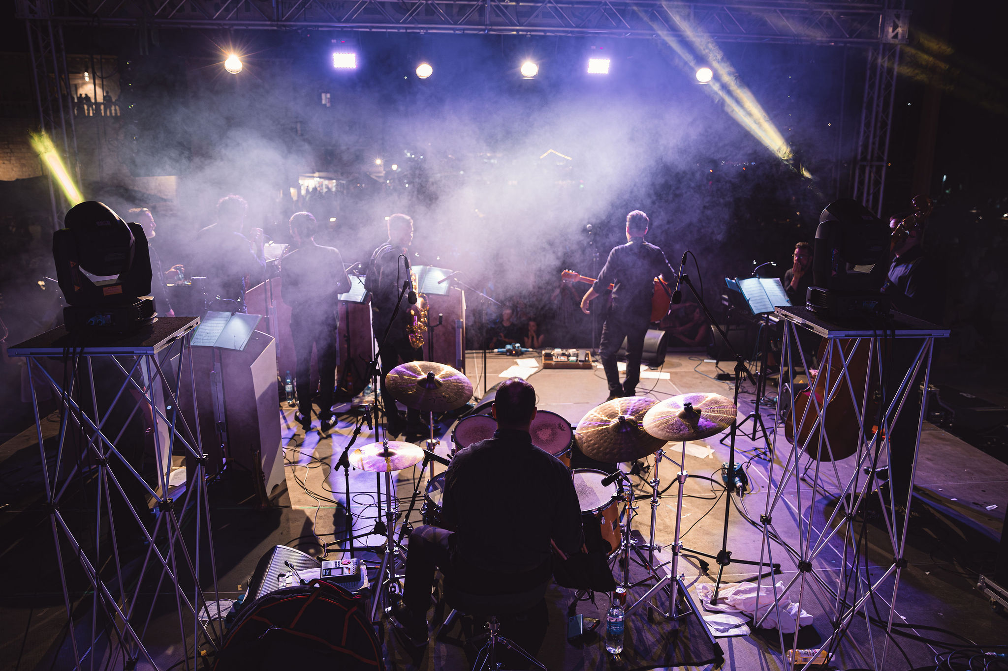Backstage view of moving head lights, truss rigging, and branded stage panels at Hvar concert production
