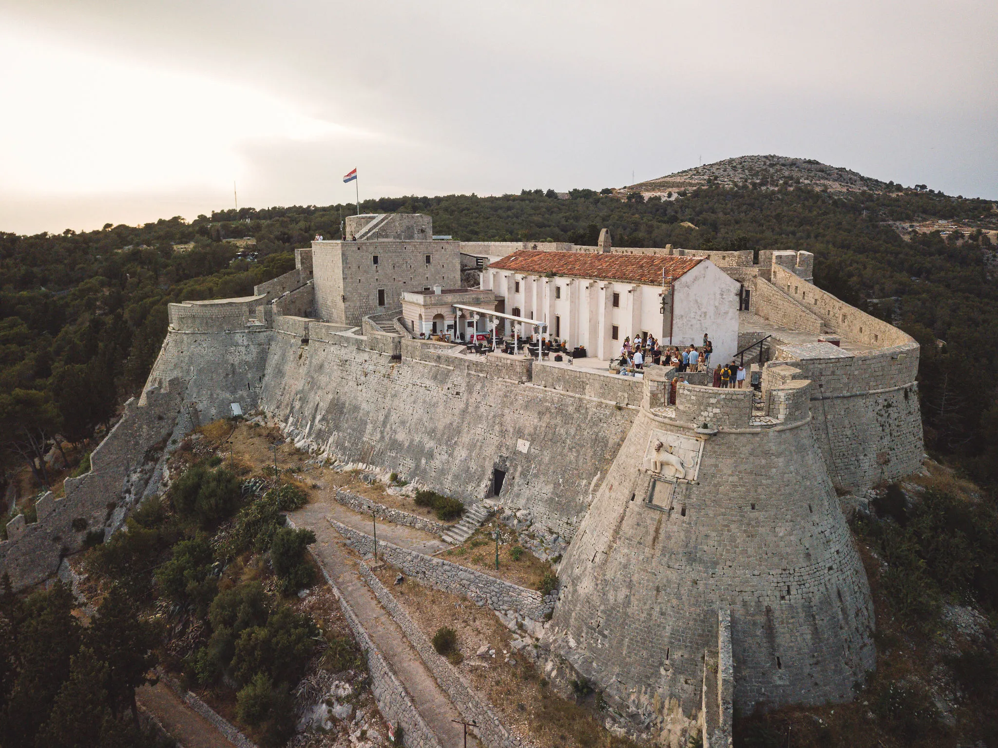 Drone aerial of Hvar fortress complex with Croatian flag and guests gathering on the terrace — Cosmic Production premium venue knowledge