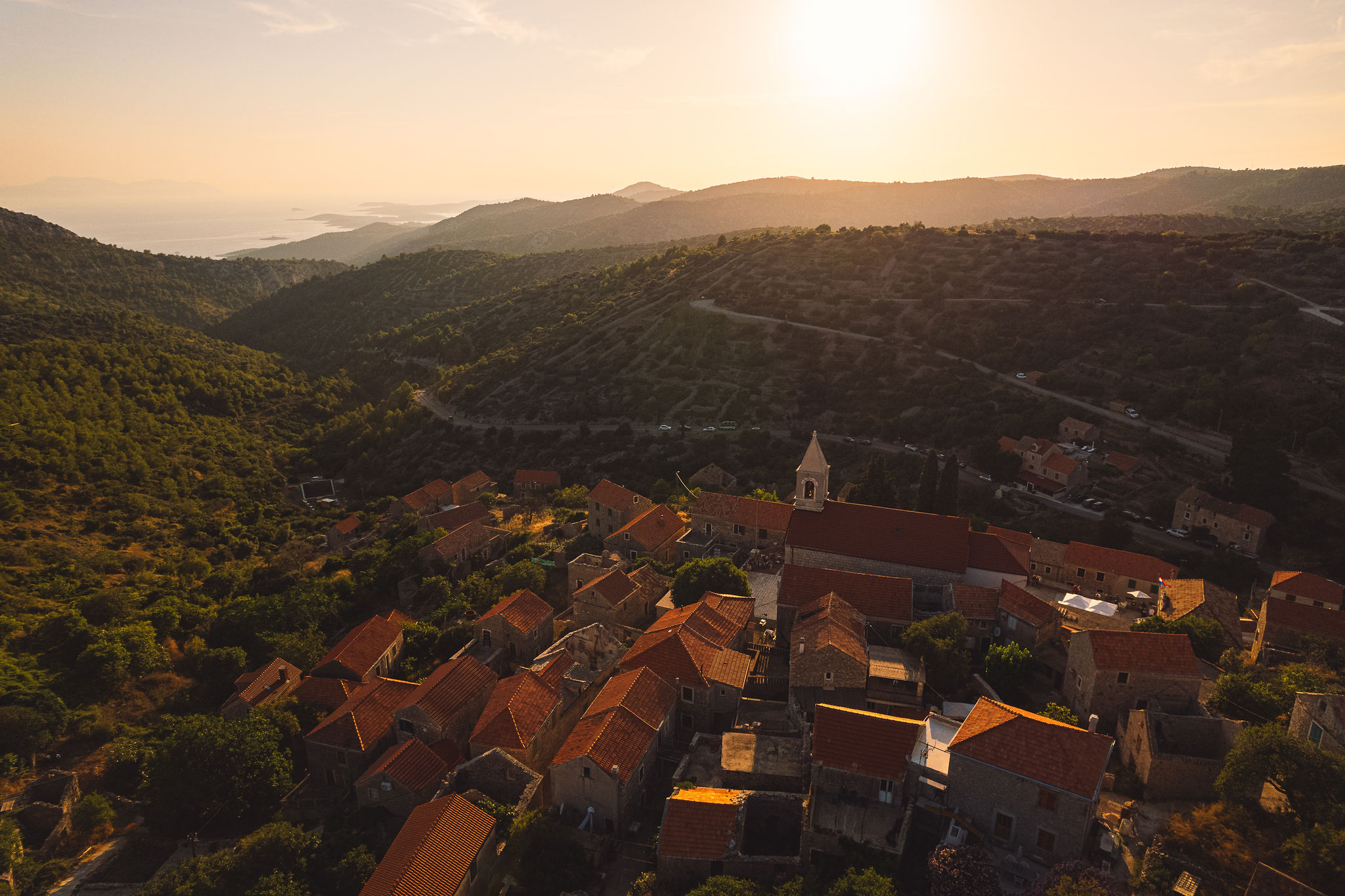 Aerial sunset view of Velo Grablje village with terracotta roofs, bell tower, and Adriatic Sea on Hvar Island